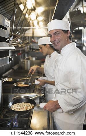 Chef and cook preparing food in commercial kitchen View Large Photo Image Stock Photo - Chef and cook preparing food in commercial kitchen. Fotosearch