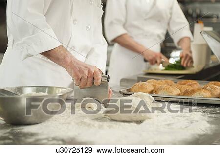 Stock Photo - Chef cutting pastry to make rolls. Fotosearch
