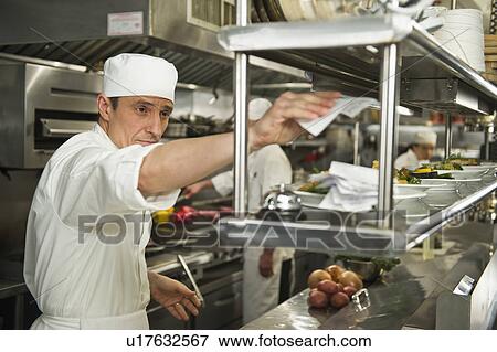 Stock Photo - Chef putting order on stick, in background chefs preparing food. Fotosearch