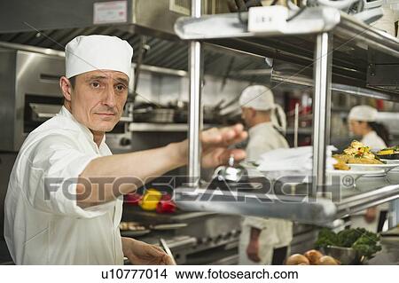 Picture - Chef ringing service bell, in background chefs preparing food. Fotosearch