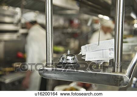 Picture - Chefs preparing food in kitchen, focus on service bell on foreground. Fotosearch