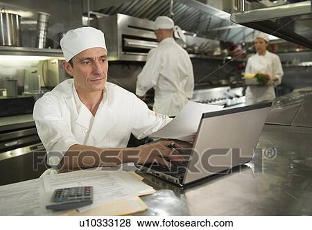 Stock Photo - Chefs preparing food, one working on laptop. Fotosearch