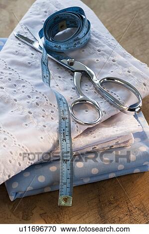 Stock Image - Close-up of folded textiles with scissors and tape measure. Fotosearch