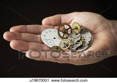 Stock Image - Close up of hand holding clock parts. Fotosearch