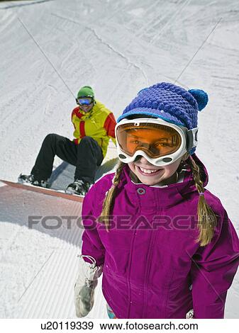 Daughter (10-11) posing with father sitting on ground with snowboard in background View Large Photo Image Stock Photo - Daughter (10-11) posing with father sitting on ground with snowboard in background . Fotosearch