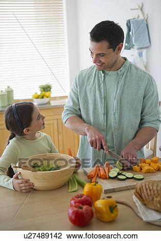 Stock Image - Daughter (8-9) and father preparing vegetables in kitchen. Fotosearch