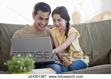 Daughter (8-9) and father sitting on sofa and using laptop View Large Photo Image Stock Photo - Daughter (8-9) and father sitting on sofa and using laptop . Fotosearch