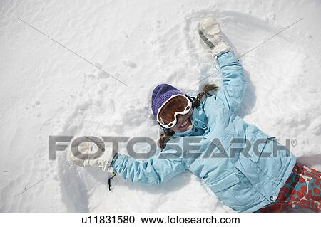 Stock Image - Girl (10-11) in ski gear doing snow angel. Fotosearch