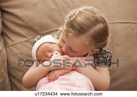 Picture - Girl (2-3) embracing baby sister on sofa. Fotosearch