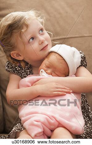 Stock Photograph - Girl (2-3) embracing baby sister on sofa. Fotosearch
