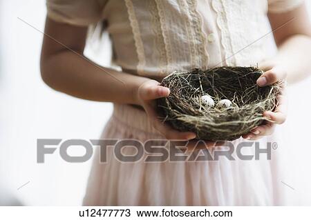 Stock Image - Girl (8-9) holding nest with small eggs. Fotosearch