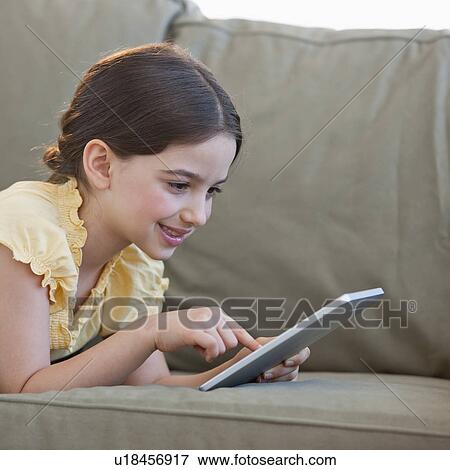 Stock Photo - Girl (8-9) lying on sofa and using digital tablet. Fotosearch