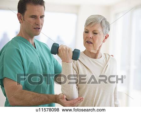 Stock Photo - Man assisting senior woman in weight lifting. Fotosearch