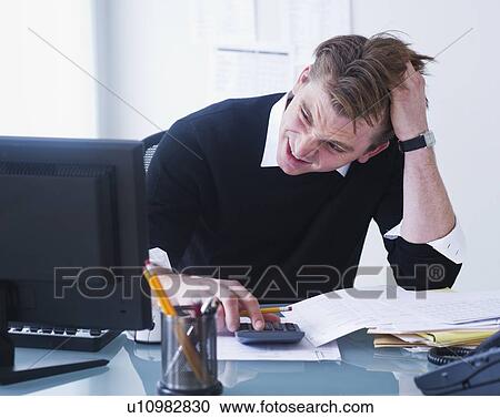 Stock Image - Man doing calculations holding head in hands. Fotosearch