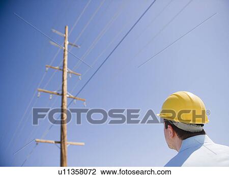 Stock Image - Man in hard hat looking at telephone pole. Fotosearch