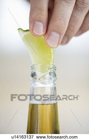 Stock Photo - Man putting lemon slice into beer bottle. Fotosearch