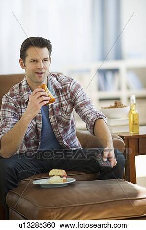Stock Image - Man watching tv and eating sandwich. Fotosearch