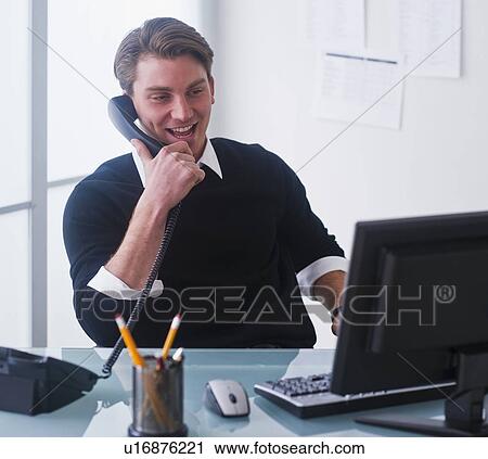 Man working on computer and talking on the phone at office View Large Photo Image Stock Image - Man working on computer and talking on the phone at office. Fotosearch