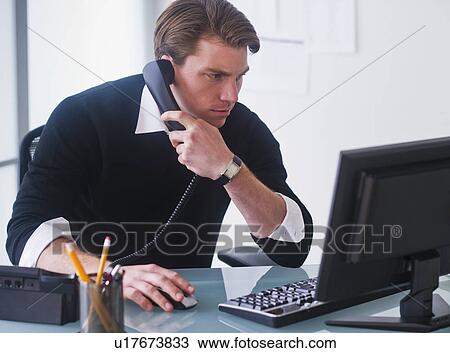 Man working on computer and talking on the phone at office View Large Photo Image Stock Image - Man working on computer and talking on the phone at office. Fotosearch