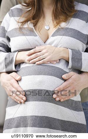 Stock Image - Man's hands on pregnant woman's belly. Fotosearch