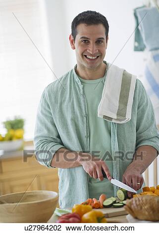 Stock Image - Mid adult man preparing vegetables in kitchen. Fotosearch