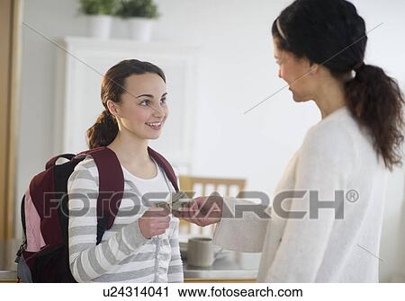 Stock Image - Mother giving money to teenage daughter (14-15). Fotosearch