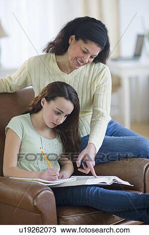 Stock Image - Mother helping to teenage girl (14-15) doing homework. Fotosearch