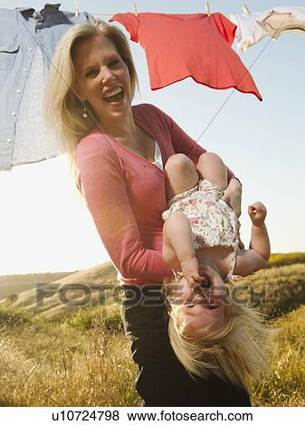 Mother playing with daughter (12-17 months) with laundry on clothesline in background View Large Photo Image Stock Photo - Mother playing with daughter (12-17 months) with laundry on clothesline in background. Fotosearch