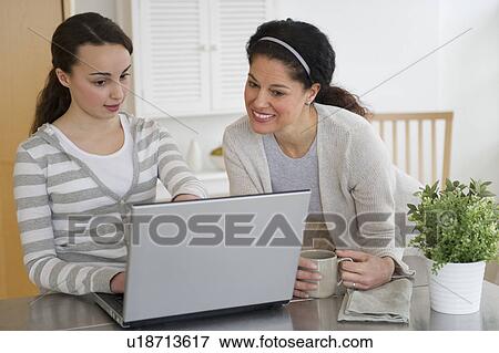Stock Photo - Mother with teenage daughter (14-15) working on laptop. Fotosearch
