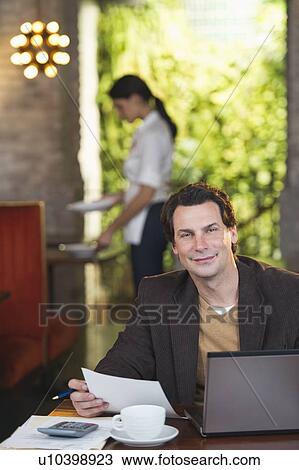 Owner working with laptop in restaurant with waitress in background View Large Photo Image Stock Image - Owner working with laptop in restaurant with waitress in background. Fotosearch