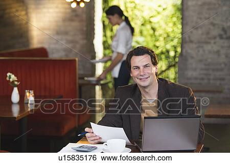 Stock Photograph - Owner working with laptop in restaurant with waitress in background. Fotosearch