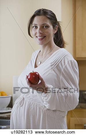 Stock Image - Portrait of expecting mother holding apple. Fotosearch