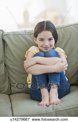 Stock Photo - Portrait of girl (8-9) sitting on sofa. Fotosearch