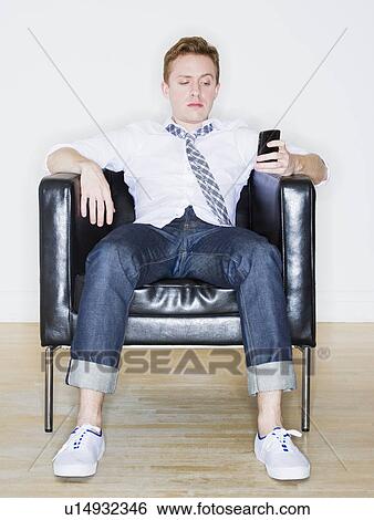 Stock Photograph - Portrait of man sitting in armchair using phone. Fotosearch