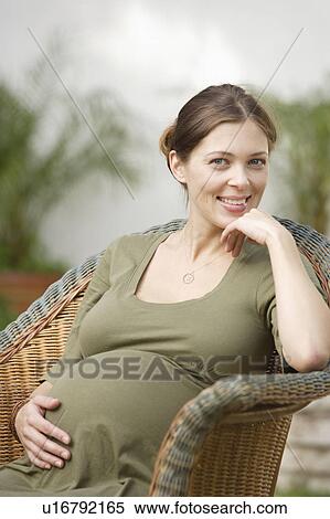 Stock Photography - Portrait of pregnant woman sitting in wicker chair. Fotosearch