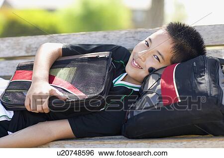 Stock Photograph - Portrait of school boy (12-13) with bags on bench. Fotosearch