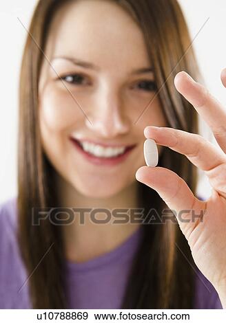 Stock Photo - Portrait of smiling young woman holding pill. Fotosearch