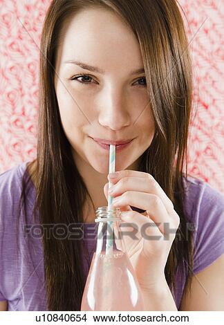 Picture - Portrait of smiling young woman drinking from bottle through straw. Fotosearch