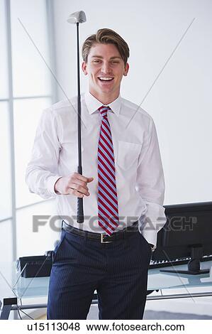 Stock Photo - Portrait of young businessman holding golf club. Fotosearch