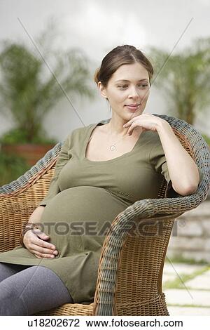 Pregnant woman sitting in wicker chair, daydreaming View Large Photo Image Stock Image - Pregnant woman sitting in wicker chair, daydreaming . Fotosearch