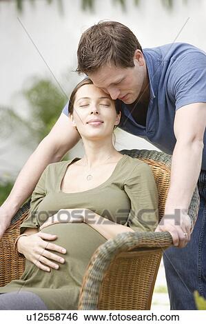 Stock Photograph - Pregnant woman sitting in wicker chair, with loving partner beside. Fotosearch