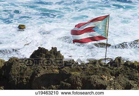 Stock Image - Puerto Rico, Old San Juan, Puerto Rican flag on rock with sea in background. Fotosearch