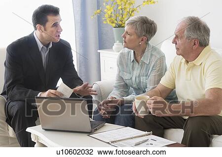 Stock Image - Senior couple talking to businessman in living room. Fotosearch