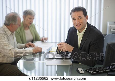 Stock Image - Senior couple talking to man in office. Fotosearch