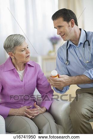 Stock Image - Smiling doctor giving medicine bottle to senior woman. Fotosearch