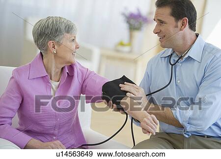 Stock Photo - Smiling man taking senior woman's blood pressure. Fotosearch
