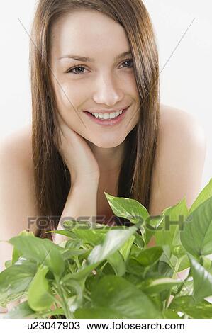 Stock Image - Studio portrait of smiling young woman with green leaves in foreground. Fotosearch