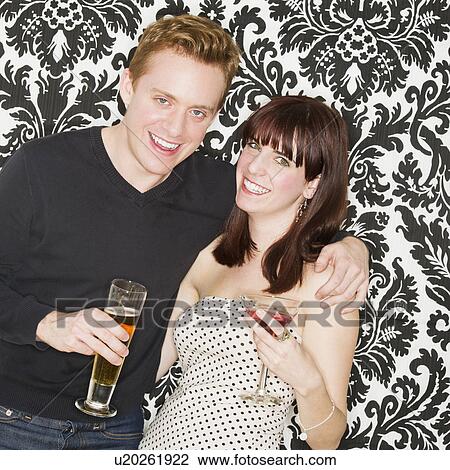 Stock Image - Studio portrait of young couple holding drinks. Fotosearch