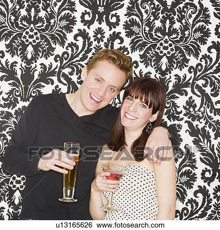 Stock Photograph - Studio portrait of young couple holding drinks. Fotosearch