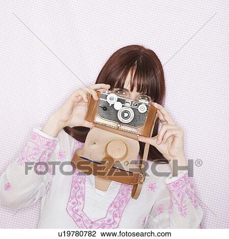 Stock Image - Studio portrait of young woman using still camera. Fotosearch